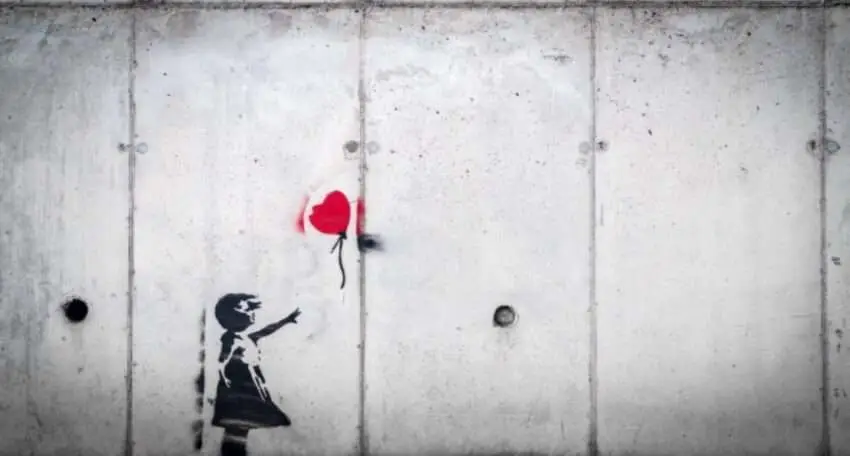 Black-and-white street art of a young girl reaching toward a red heart-shaped balloon on a concrete wall.