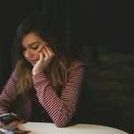 Woman at home looking at her phone with a concerned expression